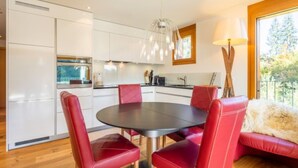 Una cocina moderna con armarios blancos, una mesa de comedor con sillas rojas y suelo de madera.