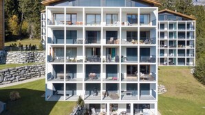 Un hotel de varios pisos con balcones, una pared de piedra y vistas a árboles.