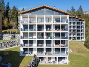 A multi-story hotel with balconies, a stone wall, and a view of trees. - Taviarna Laax 3.6 by Interhome (Laax)