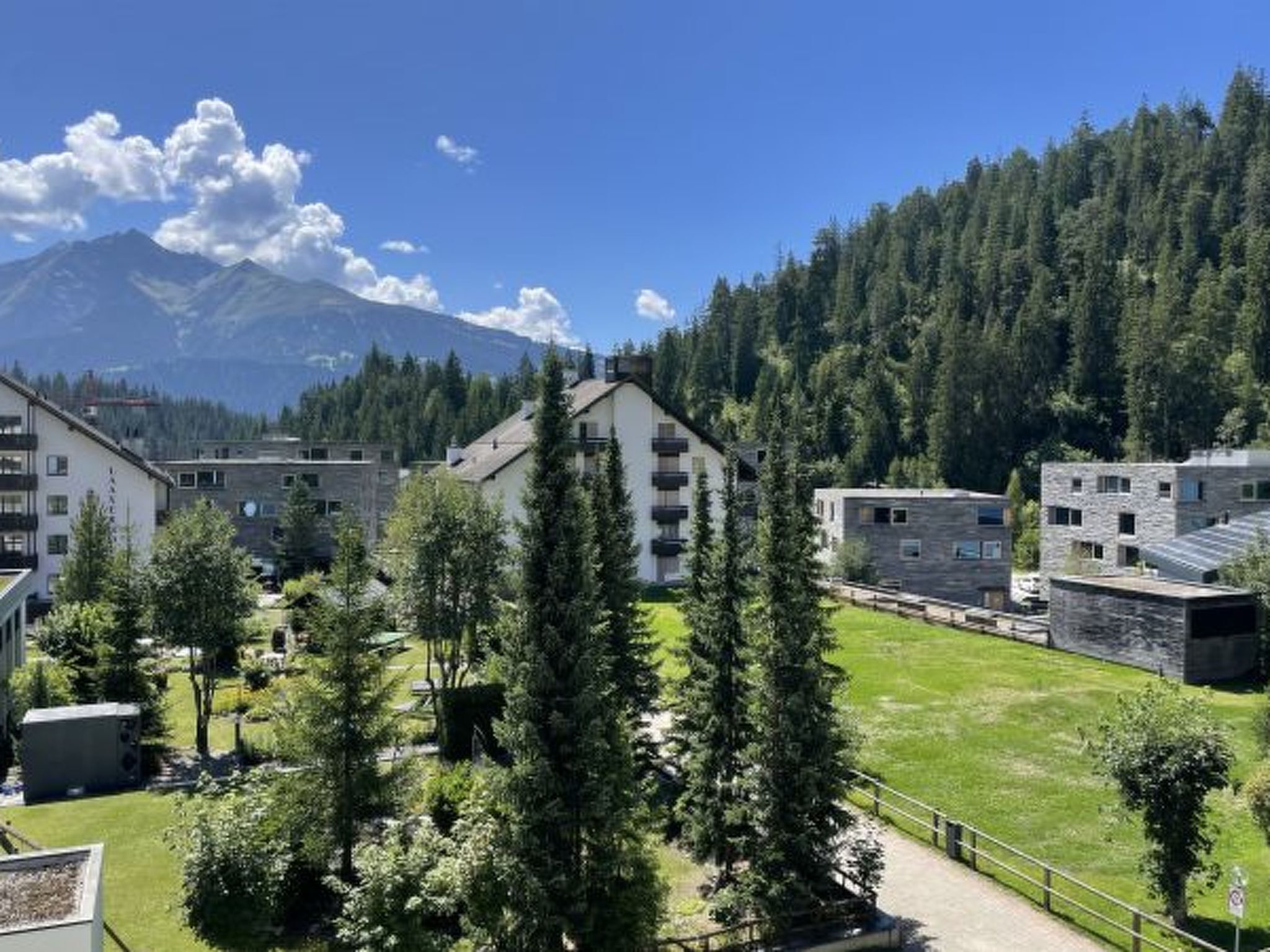 Un quartier résidentiel avec des bâtiments modernes, une montagne en arrière-plan et une forêt dense.