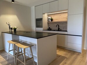 A modern kitchen with a central island, bar stools, a built-in oven, and a wooden backsplash. - Val Signina 6-21 by Interhome (Laax)