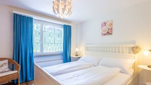 Un dormitorio con cama, una silla, ventana con cortinas, luz instalada en la pared y un objeto decorativo.