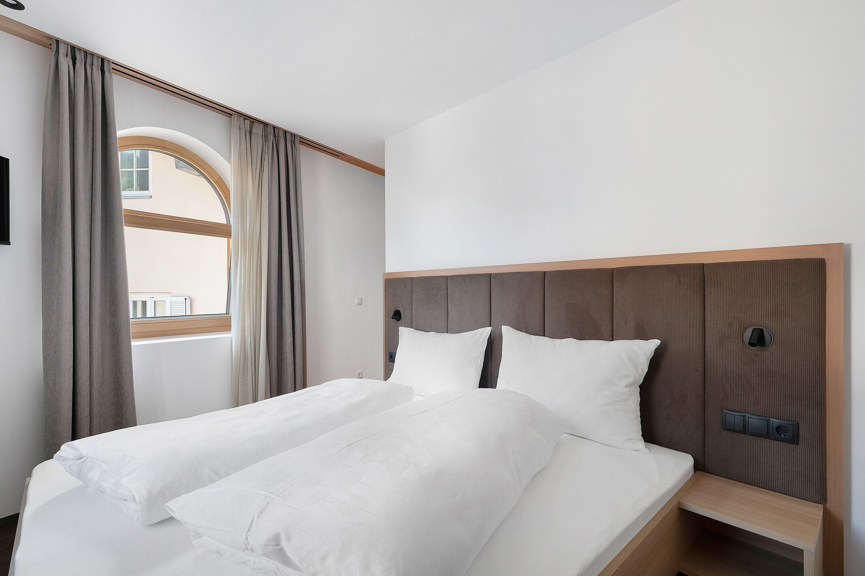 Una camera d'albergo con un letto, tende, una finestra e una testiera.