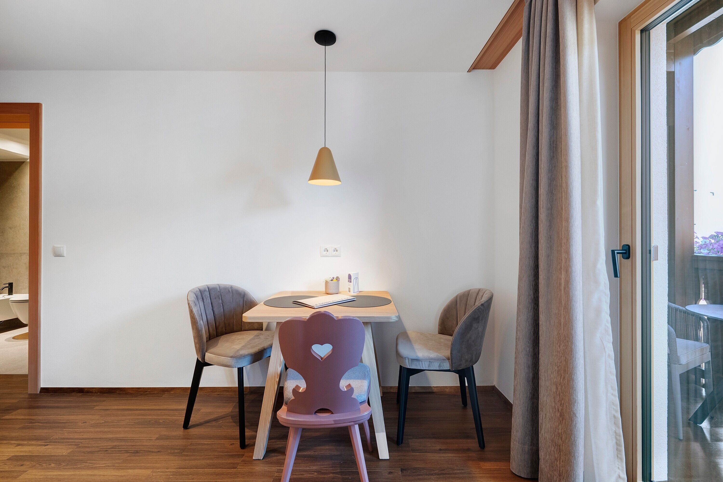 A dining area with a round table, two chairs, and a pendant light.