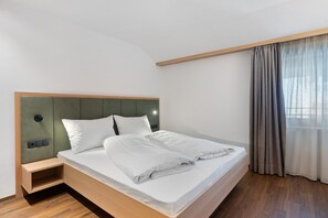 A single bed with a wooden headboard and a bedside table, a window with curtains, and a wooden floor. - Apartment 'Smart 5' with Balcony and Breakfast Included - new 2026 (Trodena nel Parco naturale)