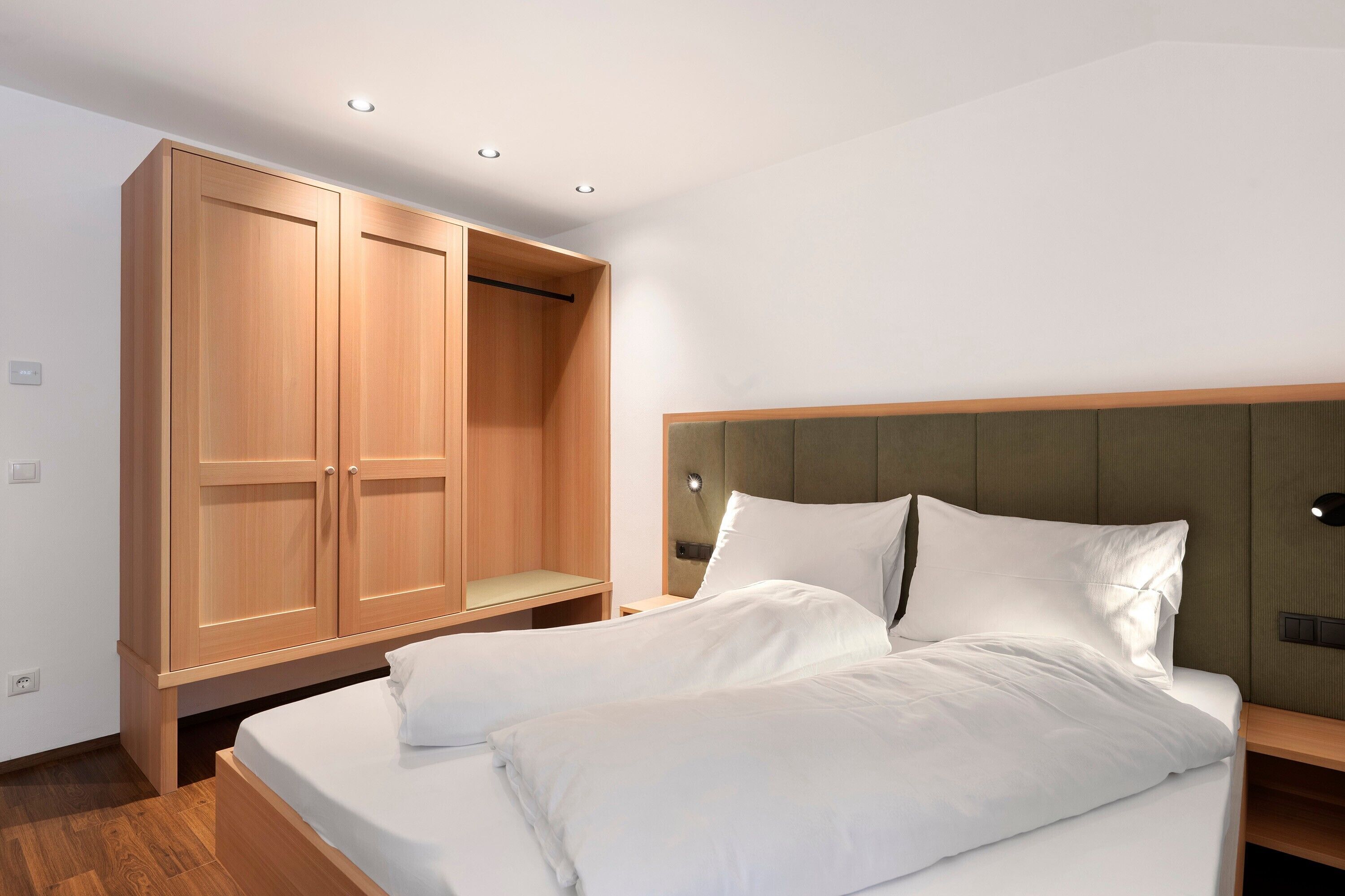 A hotel room with a bed, a wooden wardrobe, and a bedside table.