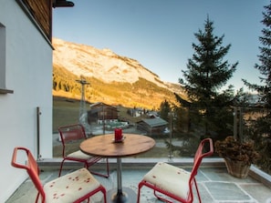 A balcony with a round table and two chairs, overlooking a mountain landscape.