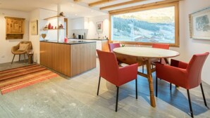 Una cocina moderna con vigas de madera, un comedor con sillas rojas y un ventanal con vistas nevadas.