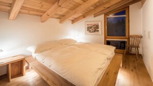 Un dormitorio con techo de madera, una cama, un ventanal y una silla.