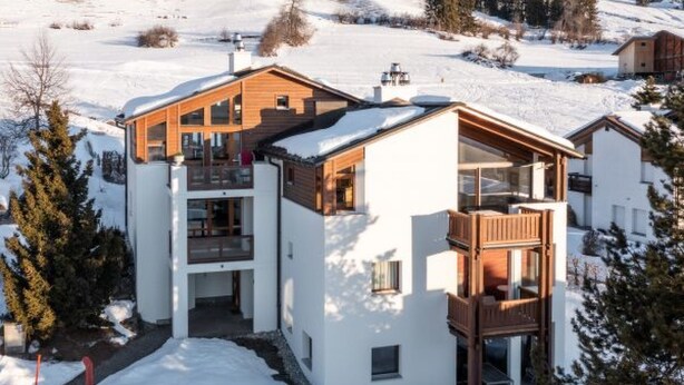 A modern multi-story building with a snow-covered landscape, wooden balconies, and a clear sky. - Casa Collina 5i-02 by Interhome (Flims)