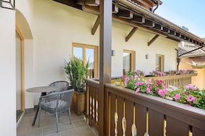 Ein Balkon mit Tisch und Stühlen, einem Blumentopf und einer Blumenkasten mit rosa Blüten.