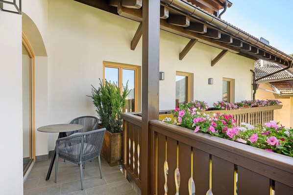 A balcony with a table and chairs, a potted plant, and a flower box with pink flowers.