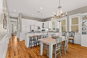 A kitchen with white cabinets, a wooden dining table, and a chandelier.