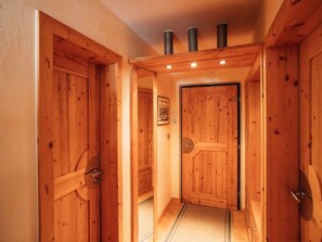 Ein Holzboden-Flur mit einer zentralen Tür, flankiert von je zwei weiteren Türen rechts und links, und einer Decke mit drei Lüftungsschlitzen.