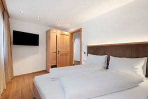 Une chambre d’hôtel avec un lit, un téléviseur fixé au mur, une armoire en bois et une porte donnant sur une autre pièce.