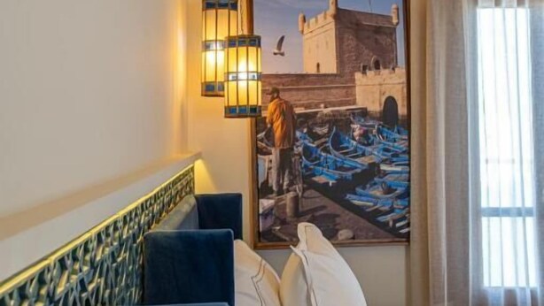 Hotelkamer met een bed, een blauwe bank, een wandlamp en een groot raam met gordijnen.