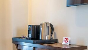 Een houten tafeltje met een koffiezetapparaat en een dienblad, een bord met een verbodsbordje, en een televisie aan de muur.