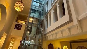 Een hotelinterieur met een glazen lift, een trap en een hoog plafond met dakramen.