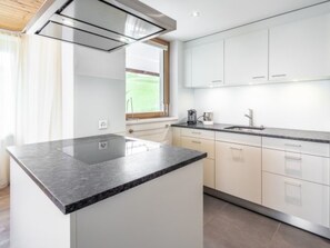 A modern kitchen with white cabinets, a granite countertop, and a window with a view of a green landscape. - Panorama Salums by Interhome (Laax)
