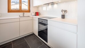 Eine moderne Küche mit weißen Schränken, einem schwarzen Backofen, einer roten Kaffeemaschine und einem Fenster mit Blick auf Gebäude.