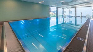 En indendørs swimmingpool med glasvægge, et loft med lineære lysarmaturer og udsigt udad.