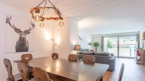 Spiseområde med et træbord og stole, en lysekrone og en stor vægdekoration af hjortegevir.