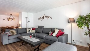 En moderne stue med en grå hjørnesofa, et sofabord og et spiseområde i baggrunden.
