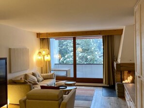 Ein Wohnzimmer mit einer Couch, einem Couchtisch, einem Kamin und einem großen Fenster mit Vorhängen.