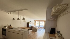 Een moderne keuken met een centraal eiland, een eethoek met een tafel en stoelen, een bank en een groot raam dat natuurlijk licht binnenlaat.