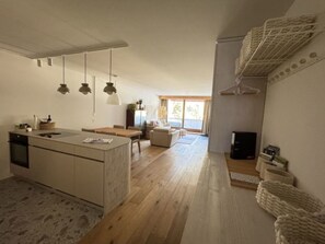 Eine moderne Küche mit einer zentralen Kochinsel, einem Essbereich mit Tisch und Stühlen, einer Couch und einem großen Fenster, das für natürliches Licht sorgt.