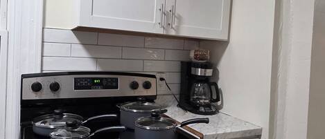 Une cuisine avec des meubles blancs, une cuisinière avec des casseroles, une machine à café et une fenêtre.