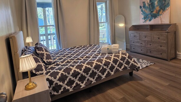 A bedroom with a bed, a nightstand, a lamp, a dresser, a mirror, and a painting.