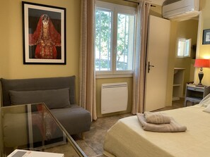 A bedroom with a bed, a grey sofa, a radiator, a window with curtains, and a framed picture on the wall. - Arts & Flores by Interhome (Carces)