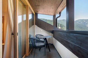 Un balcón con mesa y sillas, techo de madera y vista a una montaña boscosa.
