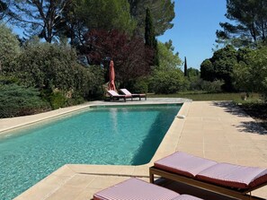 A rectangular swimming pool with clear water, surrounded by a tiled deck. There are lounge chairs with striped cushions and a single umbrella. - Vacation home Ralaye by Interhome (Carces)