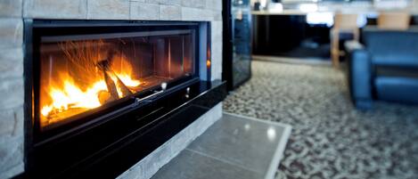 A fireplace with a stone facade, a tiled floor, and a patterned rug.