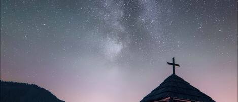 A wooden structure with a cross, surrounded by a mountainous landscape under a starry night sky.