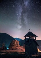 A wooden structure with a cross, surrounded by a mountainous landscape under a starry night sky.