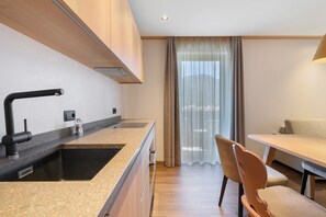 A modern kitchen with a built-in sink, a dining area with a table and chairs, and a view through a window with curtains. - Apartment 'Classic 6' with Balcony and Breakfast Included - new 2026 (Trodena nel Parco naturale)