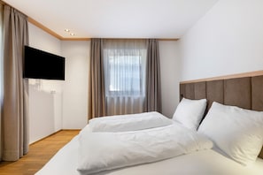 A modern hotel room with a flat-screen TV, a large bed with white linens, a wooden headboard, and a large window with sheer curtains. - Apartment 'Classic 6' with Balcony and Breakfast Included - new 2026 (Trodena nel Parco naturale)