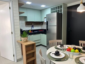 Eine moderne Küche mit hellblauen Schränken, einem Edelstahl-Kühlschrank und einem Essbereich mit einem runden Tisch für zwei Personen.