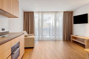 A modern living room with a kitchen area, a sofa, a TV mounted on the wall, and large windows with curtains. - Goldener Adler Apartment Comfort 8 with Balcony, Sauna and Breakfast Included - new 2026 (Trodena nel Parco naturale)