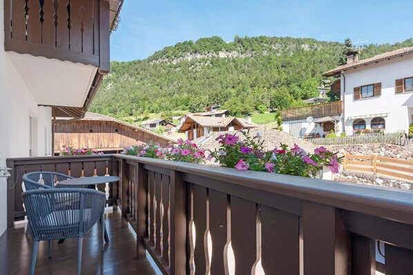 A balcony with wicker chairs, a wooden railing, and a view of a village with houses and a mountain. - Goldener Adler Apartment Comfort 8 with Balcony, Sauna and Breakfast Included - new 2026 (Trodena nel Parco naturale)