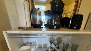 Una zona de cocina con cafetera, tazas y un recipiente rojo.
