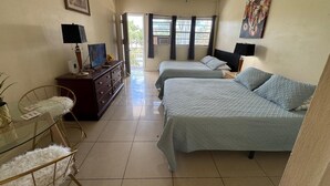 Una habitación de hotel con dos camas, un escritorio con computadora, una silla y un ventanal con cortinas.