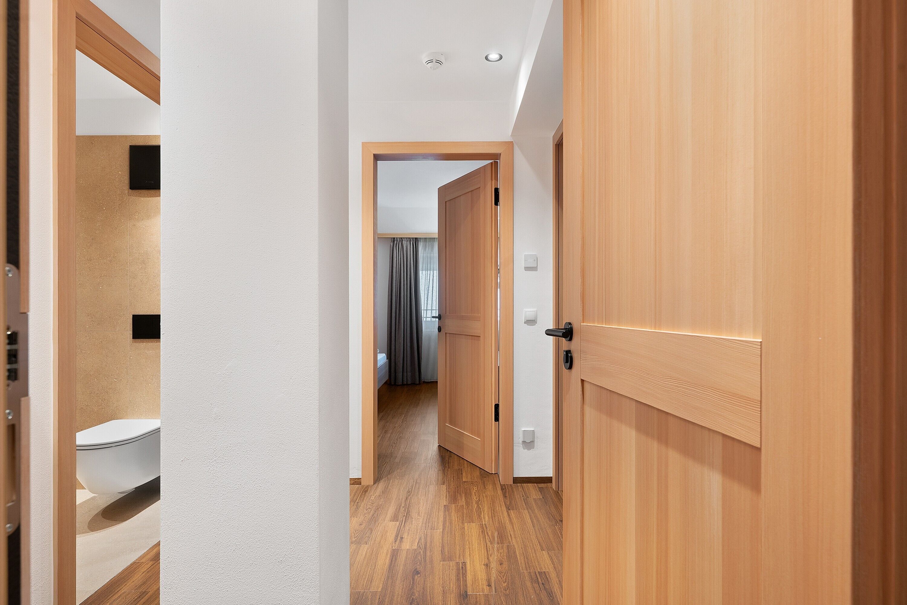 Ein Flur mit Holzboden, einer weißen Tür und einem sichtbaren Badezimmer mit Toilette.