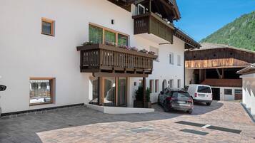 Ein zweigeschossiges Gebäude mit Balkon, ein Auto davor und ein Berg im Hintergrund.