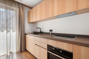 A modern kitchen with wooden cabinets, a stainless steel sink, and an oven. - Premium Apartment 4 with Balcony and Breakfast Included – new 2026 (Trodena nel Parco naturale)