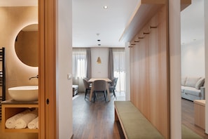A modern hotel room with a large round mirror, a wooden vanity, a dining area with a table and chairs, and a sofa. - Premium Apartment 4 with Balcony and Breakfast Included – new 2026 (Trodena nel Parco naturale)