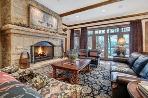 A stone fireplace, leather sofa, and a large window with curtains. - NEW! 3BR Condo in Bachelor Gulch, Ski in/out (Avon)